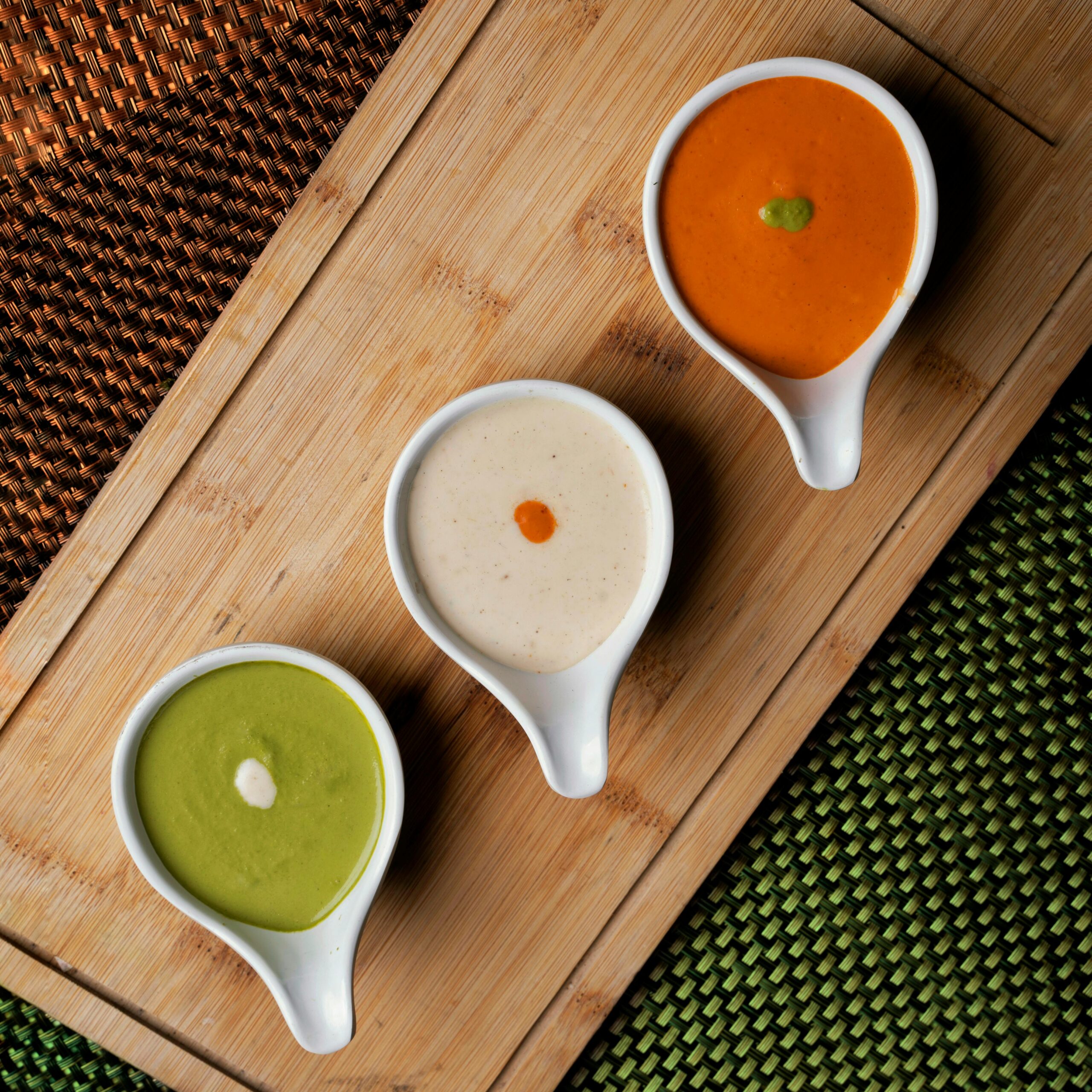 Меню Top-down view of three colorful, creamy soups in white bowls on a wooden board, showcasing vibrant culinary artistry.